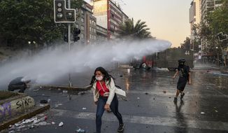 An anti-government protester walks away from the spray of a police water cannon in Santiago, Chile, Tuesday, Oct. 29, 2019. Tuesday is the 12th day of demonstrations that began with youth protests over a subway fare hike that transformed into a leaderless national movement demanding greater equality and better public services in a country long seen as an economic success story. (AP Photo/Esteban Felix)