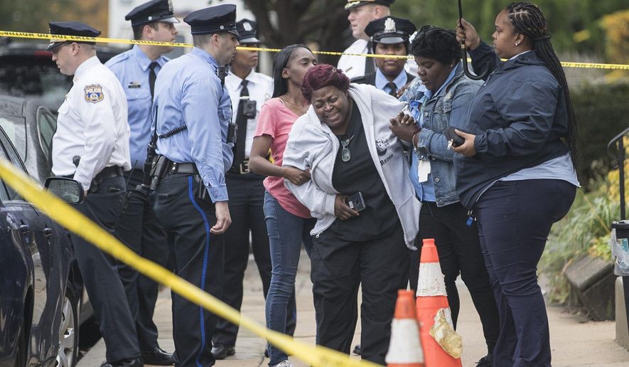 A grieving woman is assisted outside a home where four people were found shot dead Wednesday, Oct. 30, 2019, in west Philadelphia. Police say a man is in custody following the deaths of his mother, stepfather and two brothers, including a 6-year-old boy, who were found shot in the home. (Charles Fox/The Philadelphia Inquirer via AP)