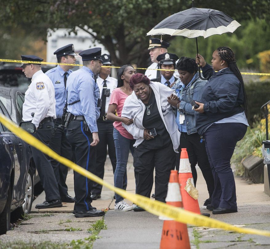 A grieving woman is assisted outside a home where four people were found shot dead Wednesday, Oct. 30, 2019, in west Philadelphia. Police say a man is in custody following the deaths of his mother, stepfather and two brothers, including a 6-year-old boy, who were found shot in the home. (Charles Fox/The Philadelphia Inquirer via AP)