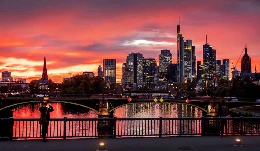 A man takes a picture of the river Main and the buildings of the banking district during sunset in Frankfurt, Germany, Monday, Oct. 21, 2019. (AP Photo/Michael Probst)