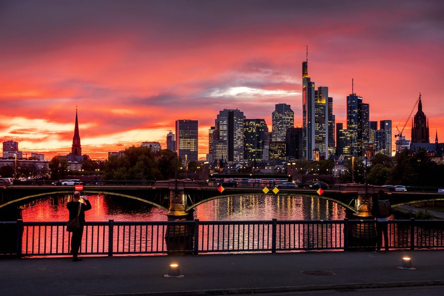 A man takes a picture of the river Main and the buildings of the banking district during sunset in Frankfurt, Germany, Monday, Oct. 21, 2019. (AP Photo/Michael Probst)