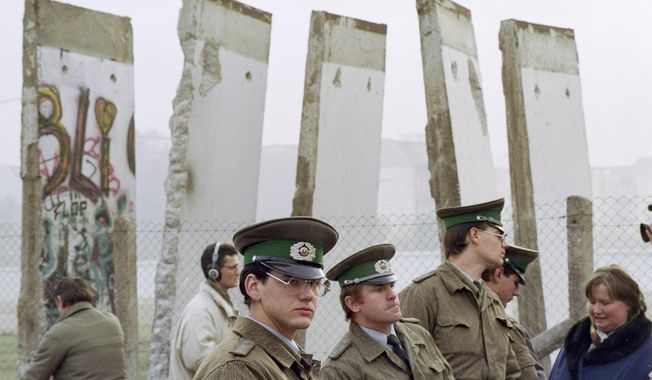 FILE - In this Monday, Nov. 13, 1989 file photo, East German border guards stand in front of segments of the Berlin Wall, which were removed to open the wall at Potsdamer Platz passage in Berlin. When the Berlin Wall fell, the Soviet Union stepped back, letting East Germany&#x27;s communist government collapse and then quickly accepting German unification. (AP Photo/John Gaps III, File)