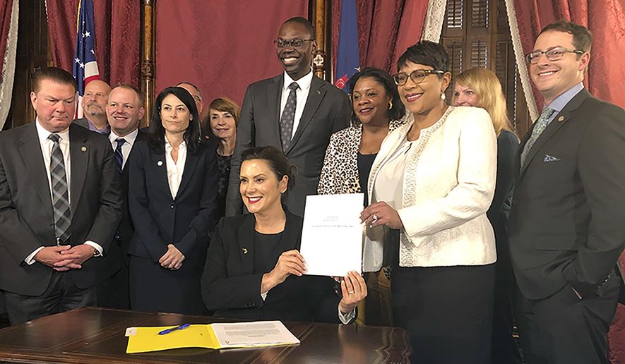 Michigan Gov. Gretchen Whitmer, flanked by lawmakers and other top state officials, displays her signature after signing bills that no longer automatically treat 17-year-old offenders as adults on Thursday, Oct. 31, 2019, at the state Capitol in Lansing, Mich. The change will take effect in 2021. (AP Photo/David Eggert)
