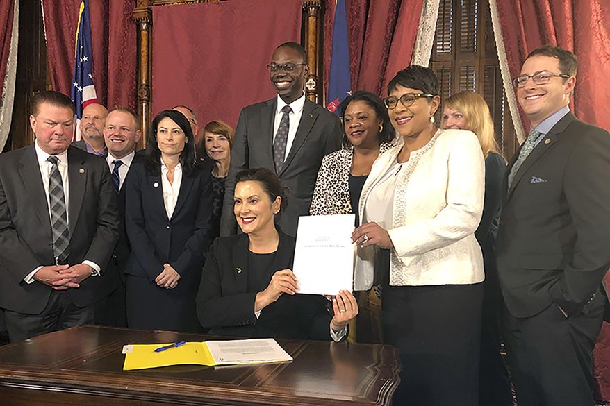 Michigan Gov. Gretchen Whitmer, flanked by lawmakers and other top state officials, displays her signature after signing bills that no longer automatically treat 17-year-old offenders as adults on Thursday, Oct. 31, 2019, at the state Capitol in Lansing, Mich. The change will take effect in 2021. (AP Photo/David Eggert)