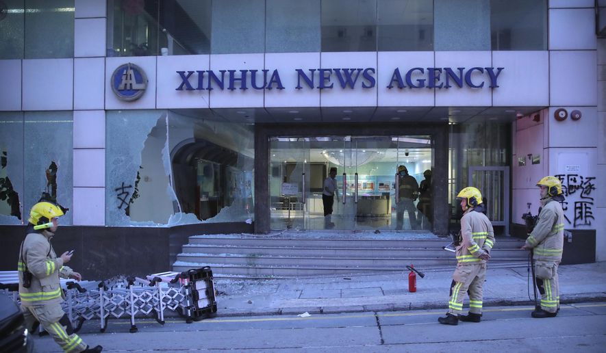 Firefighters stand outside the offices of China's Xinhua News Agency after its windows were shattered during protests in Hong Kong, Saturday, Nov. 2, 2019. Hong Kong riot police fired multiple rounds of tear gas and used a water cannon Saturday to break up a rally by thousands of masked protesters demanding meaningful autonomy after Beijing indicated it could tighten its grip on the Chinese territory. (AP Photo/Kin Cheung)