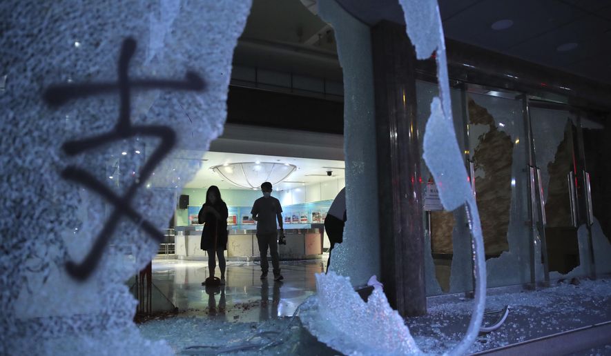 People stand in the lobby of the offices of China's Xinhua News Agency damaged by protesters in Hong Kong, Saturday, Nov. 2, 2019. Hong Kong riot police fired multiple rounds of tear gas and used a water cannon Saturday to break up a rally by thousands of masked protesters demanding meaningful autonomy after Beijing indicated it could tighten its grip on the Chinese territory. (AP Photo/Kin Cheung)