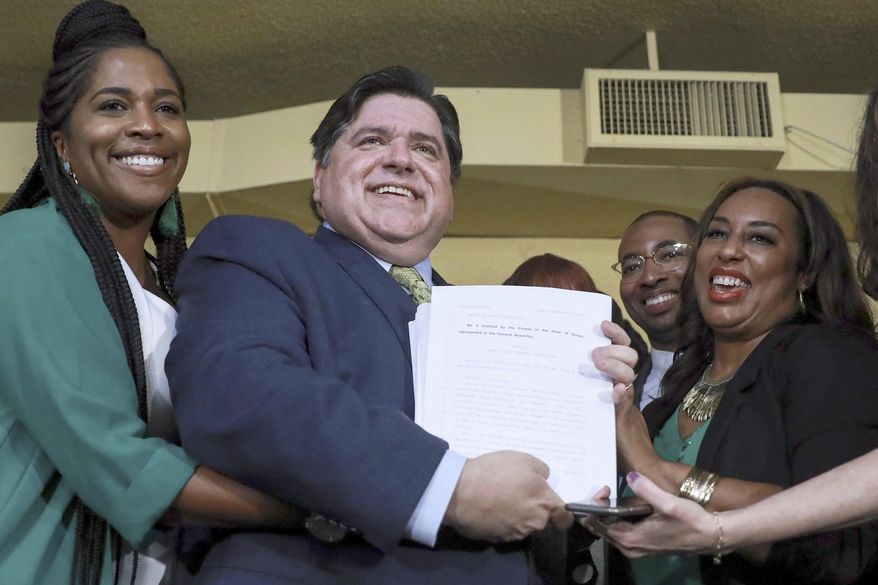 FILE - In this June 25, 2019 file photo, Gov. J. B. Pritzker holds a bill that legalizes adult-use cannabis in the state of Illinois accompanied by state Rep. Kelly Cassidy, left, and state Sen. Toi Hutchinson, right, in Chicago. Illinois becomes the 11th to legalize the adult-use of recreational marijuana. Like in other states before it, advocates of legalizing recreational marijuana use in Illinois want the law to look backward as well as forward. It conscientiously attempts to ensure that those who profit from growing and selling the weed have substantial representation from the mostly impoverished neighborhoods nailed the hardest by decades of drug crackdowns. (AP Photo/Amr Alfiky File)
