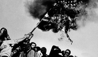 FILE - In this Nov. 9, 1979 file photo, demonstrators burn an American flag atop the wall of the U.S. Embassy in Tehran, Iran, where students have been holding American hostages. Nov. 4, 2019, will mark the 40th anniversary of the start of the 444-day hostage crisis that soured relations between the U.S. and the Islamic Republic for decades to come. (AP Photo/Thierry Campion, File)
