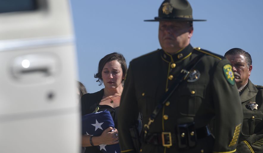 Katie Kregoski Ishmael, left, wife of fallen El Dorado County Sheriff's Deputy Brian Ishmael, holds a flag while her husband's casket is placed in a hearse at Bayside Adventure Church in Roseville, Calif., Tuesday, Nov. 5, 2019. El Dorado County Sheriff John D'Agostini stands at the far right. Friends, colleagues and family on Tuesday remembered a Northern California sheriff's deputy killed last month while responding to a call about a theft from a marijuana garden as a devoted father and a committed deputy. More than 3,000 people attended a service in honor of Deputy Ishmael. Blue ribbons were tied to the trees lining the road to the church, and adorned the doors leading to the church's sanctuary, The Sacramento Bee reported. (Daniel Kim/The Sacramento Bee via AP)