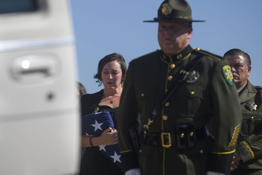 Katie Kregoski Ishmael, left, wife of fallen El Dorado County Sheriff's Deputy Brian Ishmael, holds a flag while her husband's casket is placed in a hearse at Bayside Adventure Church in Roseville, Calif., Tuesday, Nov. 5, 2019. El Dorado County Sheriff John D'Agostini stands at the far right. Friends, colleagues and family on Tuesday remembered a Northern California sheriff's deputy killed last month while responding to a call about a theft from a marijuana garden as a devoted father and a committed deputy. More than 3,000 people attended a service in honor of Deputy Ishmael. Blue ribbons were tied to the trees lining the road to the church, and adorned the doors leading to the church's sanctuary, The Sacramento Bee reported. (Daniel Kim/The Sacramento Bee via AP)