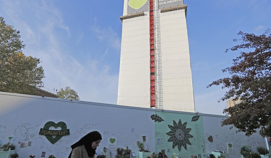 A woman passes a construction wall with written messages near Grenfell Tower in London, Wednesday, Oct. 30, 2019. A report released Wednesday on the deadly apartment block fire in London has condemned the London Fire Brigade and concluded that fewer people would have died if the building were evacuated more quickly. (AP Photo/Frank Augstein)