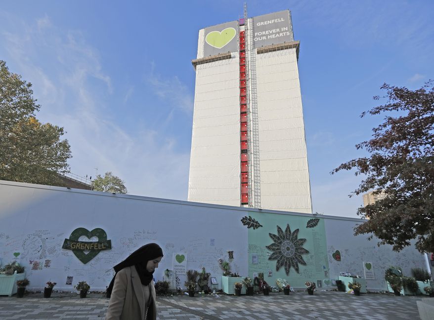 A woman passes a construction wall with written messages near Grenfell Tower in London, Wednesday, Oct. 30, 2019. A report released Wednesday on the deadly apartment block fire in London has condemned the London Fire Brigade and concluded that fewer people would have died if the building were evacuated more quickly. (AP Photo/Frank Augstein)