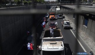 A demonstrator waves a Chilean national flag while atop a truck during a protest against highway tolls, in Santiago, Chile,Wednesday, Nov. 6, 2019. Chilean President Sebastián Piñera has proposed to Congress a 16% increase in the minimum wage while hundreds of cars traveled by caravan demanding a reduction in tolls. (AP Photo/Esteban Felix)
