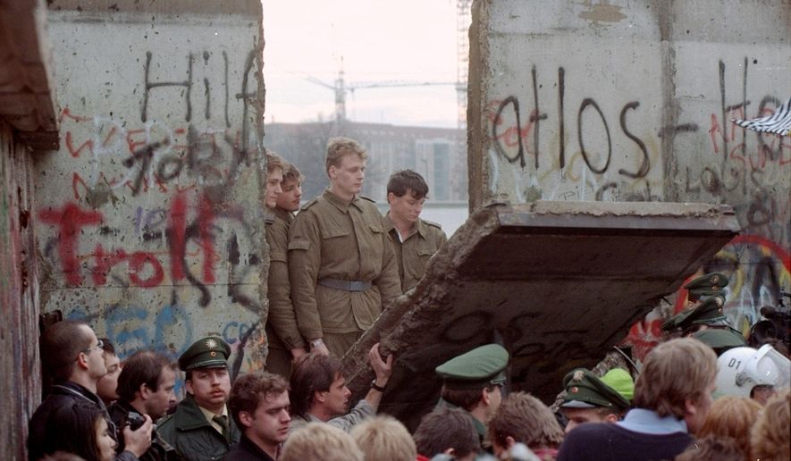 In this Saturday, Nov. 11, 1989, file photo, East German border guards are seen through a gap in the Berlin Wall after demonstrators pulled down a segment of the wall at the Brandenburg Gate, Berlin. (AP Photo/Lionel Cironneau, File)