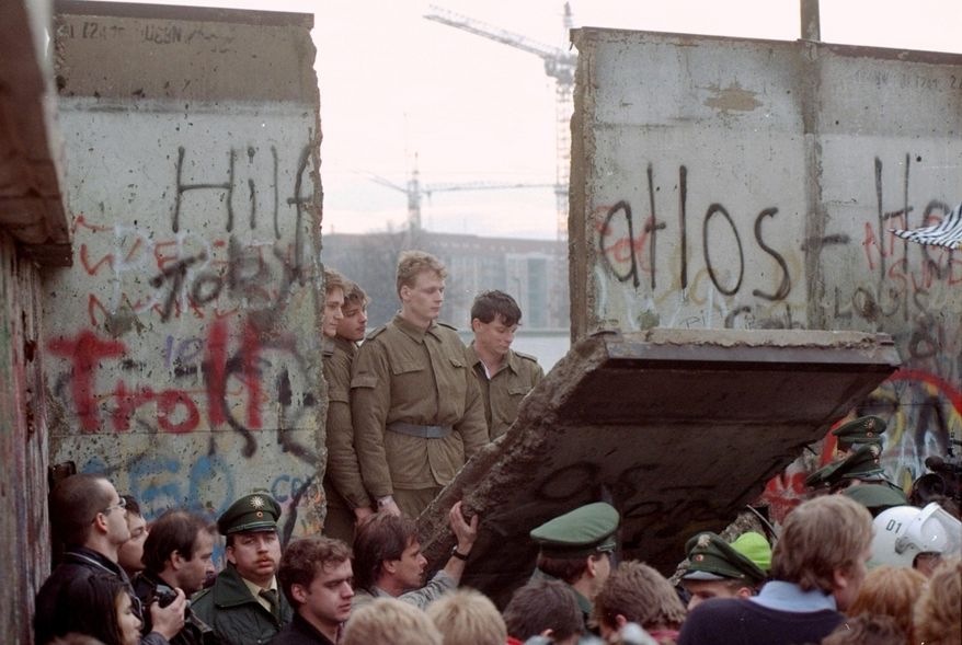 In this Saturday, Nov. 11, 1989, file photo, East German border guards are seen through a gap in the Berlin Wall after demonstrators pulled down a segment of the wall at the Brandenburg Gate, Berlin. (AP Photo/Lionel Cironneau, File)