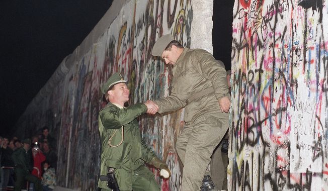 FILE - In this Sunday Nov. 12, 1989 file photo, West German policeman, left, gives a helping hand to an East German border guard who climbs through a gap of the Berlin Wall when East Germany opened another passage at Potsdamer Platz in Berlin. (AP Photo/Thomas Kienzle)