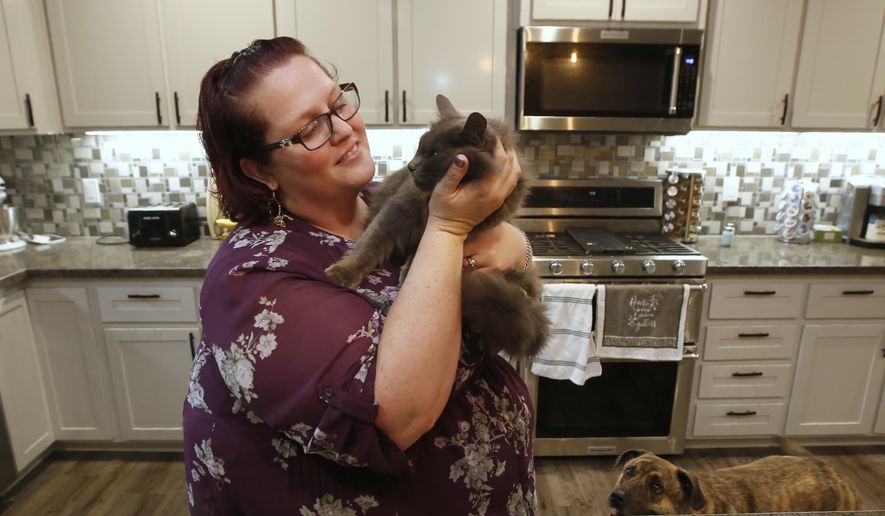 Victoria Sinclaire holds her cat Toby, that survived the Camp Fire, as her dog Joey looks on at her recently rebuilt home in Paradise, Calif., Tuesday, Nov. 5, 2019. Unable to get Toby and another of her pet cats, it took Sinclaire six hours to escape the flames from last year's wildfire that destroyed 90 percent of Paradise. (AP Photo/Rich Pedroncelli)