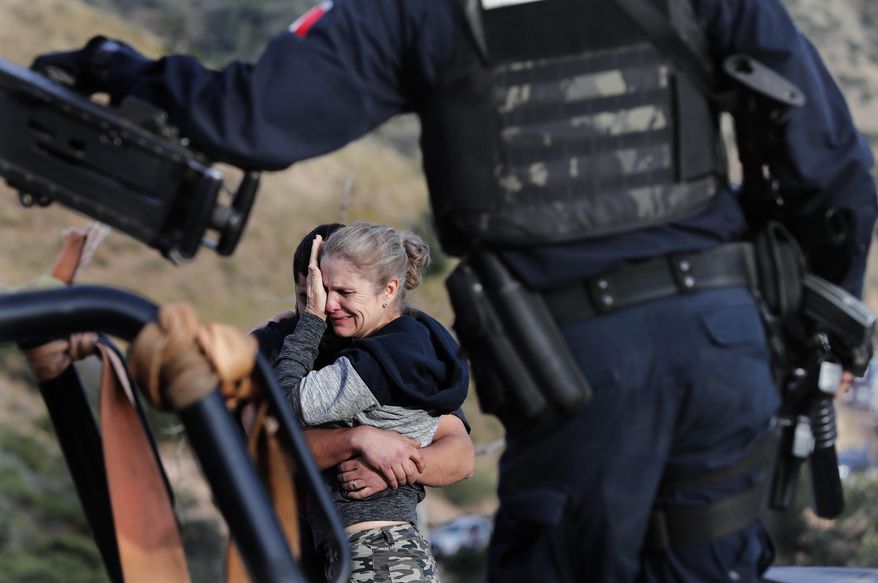 Framed by heavily armed Mexican authorities, relatives of the LeBaron family mourn at the site where nine U.S. citizens, three women and six children related to the extended LeBaron family, were slaughtered when cartel gunmen ambushed three SUVs along a dirt road near Bavispe, at the Sonora-Chihuahua border, Mexico, Wednesday, Nov 6, 2019. Three women and six of their children, related to the extended LeBaron family, were gunned down in an attack while traveling along Mexico's Chihuahua and Sonora state border on Monday. (AP Photo/Marco Ugarte)