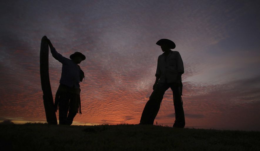 FILE - In this May 18, 2017 file photo, Joao Aquino Pereira, right, talks with fellow cowboy Rene Almeida at dawn in Corumba, in the Pantanal wetlands of Mato Grosso do Sul state, Brazil. As of Wednesday, Nov. 6 2019, fires in Brazil's Pantanal wetlands have ripped through the biodiverse region, consuming 15,000 football fields of vegetation in just the past 10 days, burning some animals alive and sending others fleeing. (AP Photo/Eraldo Peres, File)
