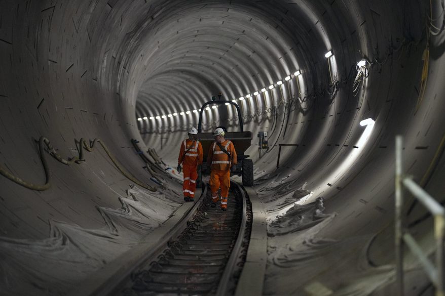 FILE - In this Wednesday, April 22, 2015 file photo, people walk along a Crossrail tunnel that heads off in a north easterly direction towards Stratford from the Stepney Green shaft in east London. The planned opening of London's new east-west railway, Crossrail, was delayed again Friday, Nov. 8, 2019 as costs increased by up to 650 million pounds ($832 million). The 73-mile (118-kilometer) line, which will be formally known as the Elizabeth Line - after Queen Elizabeth II - is Britain's biggest infrastructure project in decades. (AP Photo/Matt Dunham, file)