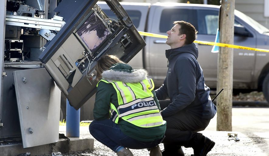 Police officers investigate an automated teller machine that exploded at the First Security Bank in Missoula, Mont., Thursday, Nov. 7, 2019. Two people have been detained. Witnesses reported seeing a man in a gray minivan pour liquid on the ATM and ignite it, causing an explosion. The ATM was damaged, but no injuries were reported. (Tommy Martino/The Missoulian via AP)