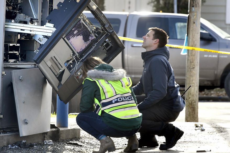 Police officers investigate an automated teller machine that exploded at the First Security Bank in Missoula, Mont., Thursday, Nov. 7, 2019. Two people have been detained. Witnesses reported seeing a man in a gray minivan pour liquid on the ATM and ignite it, causing an explosion. The ATM was damaged, but no injuries were reported. (Tommy Martino/The Missoulian via AP)