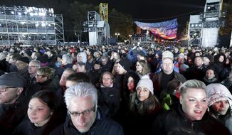 Visitors stay in front of the Brandenburg Gate as they attend stage presentations to celebrate the 30th anniversary of the fall of the Berlin Wall in Berlin, Germany, Saturday, Nov. 9, 2019. (AP Photo/Michael Sohn)