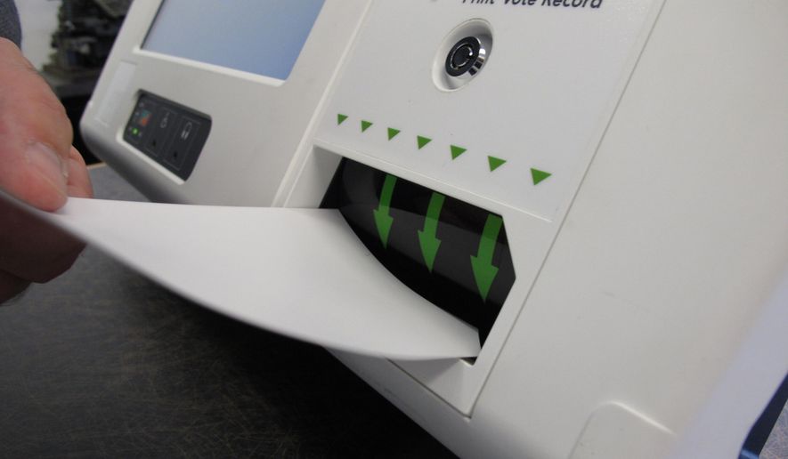 FILE - In this Aug. 16, 2019, file photo, a man feeds a ballot card into a digital voting machine during a demonstration in Raleigh, N.C. A new report says the nation’s elections are vulnerable to attack due to a lack of robust federal oversight of the private companies that are involved in everything from manufacturing voting systems to maintaining voter registration databases (AP Photo/Allen G. Breed, File)