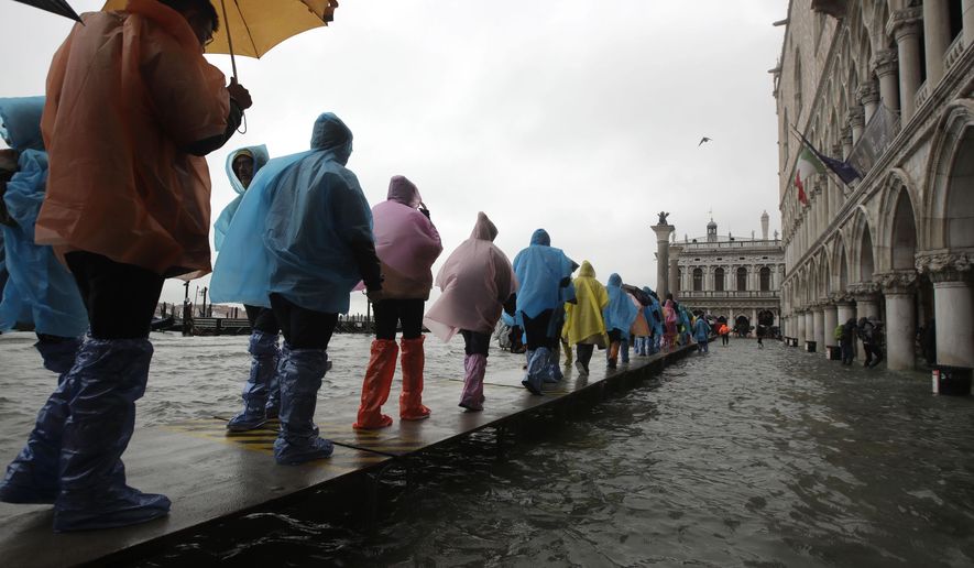 People walk on catwalk set up on the occasion of a high tide, in a flooded Venice, Italy, Tuesday, Nov. 12, 2019. The high tide reached a peak of 127cm (4.1ft) at 10:35am while an even higher level of 140cm(4.6ft) was predicted for later Tuesday evening. (AP Photo/Luca Bruno)