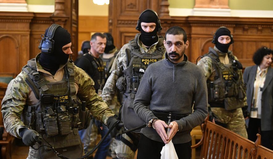 A Syrian man identified as Hassan F., centre, is escorted by Police officers as he arrives at the Metropolitan Court in Budapest, Hungary, Wednesday, Nov. 13, 2019. Prosecutors said the 27-year-old man identified only as Hassan F. participated in the beheading of a religious leader in the city of al-Sukhnah in Homs province and was also involved in the killings of at least 25 people. (Zsolt Szigetvary/MTI via AP)