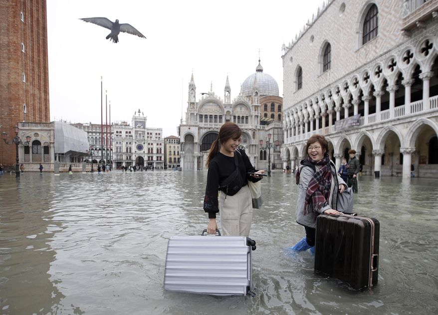 Tourists push their luggage in a flooded St. Mark's Square, in Venice, Nov. 13, 2019. (AP Photo/Luca Bruno)