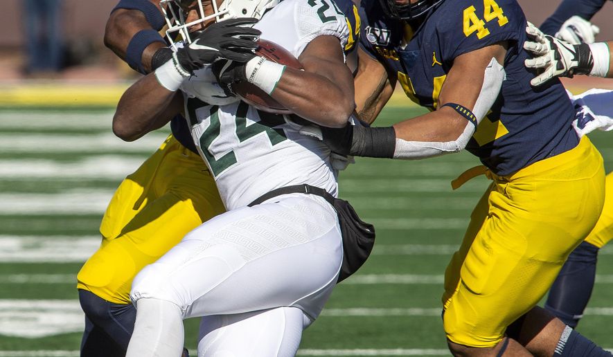Michigan State running back Elijah Collins (24) gets tackled by Michigan defensive back Josh Metellus, top left, and linebacker Cameron McGrone (44) in the first quarter of an NCAA college football game in Ann Arbor, Mich., Saturday, Nov. 16, 2019. Michigan won 44-10. (AP Photo/Tony Ding)
