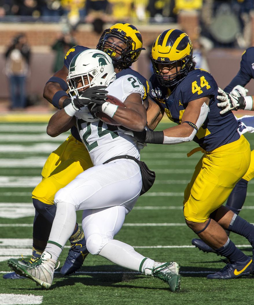Michigan State running back Elijah Collins (24) gets tackled by Michigan defensive back Josh Metellus, top left, and linebacker Cameron McGrone (44) in the first quarter of an NCAA college football game in Ann Arbor, Mich., Saturday, Nov. 16, 2019. Michigan won 44-10. (AP Photo/Tony Ding)