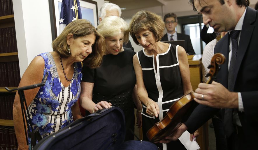 FILE - In an August 6, 2015 file photo, FBI agent Chris McKeogh, right, shows sisters Amy Totenberg, left, Nina Totenberg, second from left, and Jill Totenberg the Ames Stradivarius violin that was stolen from their father 35 year ago, in New York. The Stradivarius violin stolen four decades ago from the late virtuoso Roman Totenberg and returned to his family by a federal prosecutor came alive again _ at the crime scene, playing the same music. At a concert in Cambridge, Massachusetts, 19-year-old star violinist Nathan Meltzer revived the priceless instrument of the Polish-born musician on Friday evening, Nov. 15, 2019.   (AP Photo/Seth Wenig, File)