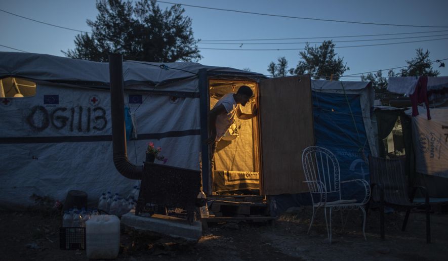 In this Thursday Oct. 3, 2019 photo, an Afghan man looks out of his tent in a makeshift refugee and migrant camp on the fringes of the overcrowded Moria camp on the Greek island of Lesbos. Greece's conservative government announced Wednesday Nov. 20, 2019, plans to overhaul the country's migration management system, and replacing existing camps on the islands with detention facilities and moving and 20,000 asylum seekers to the mainland over the next few weeks. (AP Photo/Petros Giannakouris)