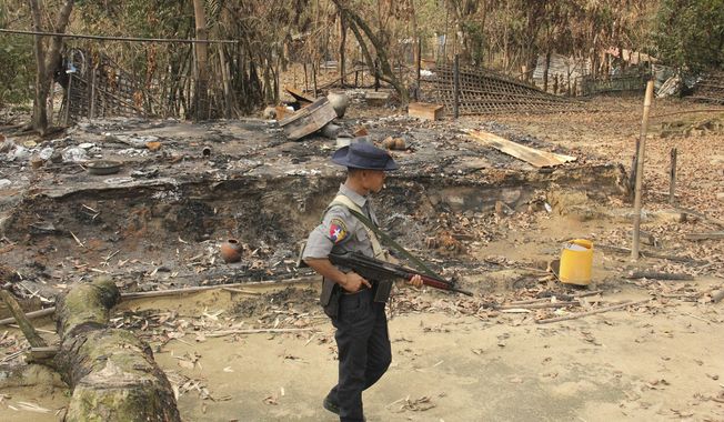 FILE - In this Sept. 6, 2017, file photo, a Myanmar security officer walks past burned Rohingya houses in Ka Nyin Tan village of suburb Maungdaw, northern Rakhine state of western Myanmar. Myanmar’s government announced Wednesday, Nov. 20, 2019 that its leader, Aung San Suu Kyi, will head a legal team it will send to the International Court of Justice in the Netherlands to contest a case of genocide filed against it by Gambia on behalf of the Organization of Islamic Cooperation. (AP Photo, File)