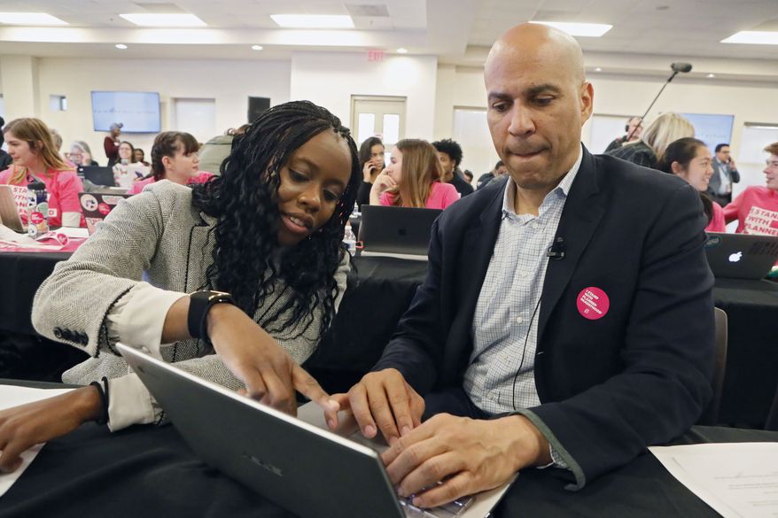 Democratic presidential candidate Sen. Cory Booker, D-J., right, gets some assistance from Esosa Osa while texting people on a call list as he participates in at a Fair Fight phone bank at Ebenezer Baptist Church, Thursday, Nov. 21, 2019, in Atlanta. Democratic presidential candidates including Cory Booker, Amy Klobuchar, Andrew Yang and Pete Buttigieg, along with Stacey Abrams, joined in at the phone bank in response to Georgia election officials&#39; plan to cancel more than 313,000 voter registrations next month. (Bob Andres/Atlanta Journal-Constitution via AP)