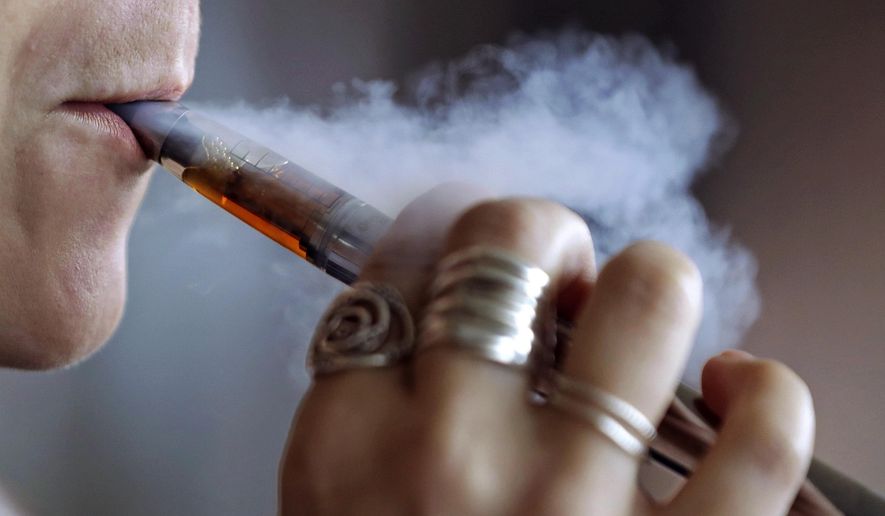 FILE - In this Friday, Oct. 4, 2019 file photo, a woman using an electronic cigarette exhales a puff of smoke in Mayfield Heights, Ohio. Massachusetts lawmakers have approved the nation's toughest restrictions on flavored tobacco and vaping products, including menthol cigarettes. The ban was passed by the Senate early Thursday, Nov. 21, before the legislature broke for a holiday recess. It had earlier been passed by the state House of Representatives. (AP Photo/Tony Dejak)