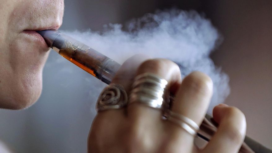FILE - In this Friday, Oct. 4, 2019 file photo, a woman using an electronic cigarette exhales a puff of smoke in Mayfield Heights, Ohio. Massachusetts lawmakers have approved the nation's toughest restrictions on flavored tobacco and vaping products, including menthol cigarettes. The ban was passed by the Senate early Thursday, Nov. 21, before the legislature broke for a holiday recess. It had earlier been passed by the state House of Representatives. (AP Photo/Tony Dejak)