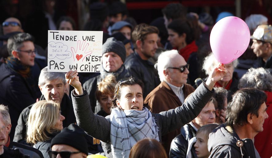 This Jan. 4, 2017 photo shows a woman holding a placard reading "Holding one's hand out is not a crime", as she supports Cedric Herrou, a French activist farmer who faces up to five years in prison as he goes on trial accused of helping African migrants cross the border from Italy, in Nice, southern France. A French appeals court is expected to hand down a verdict Thursday afternoon in the case of a mountain guide who was convicted for helping migrants enter the country illegally. (AP Photo/Claude Paris, File)