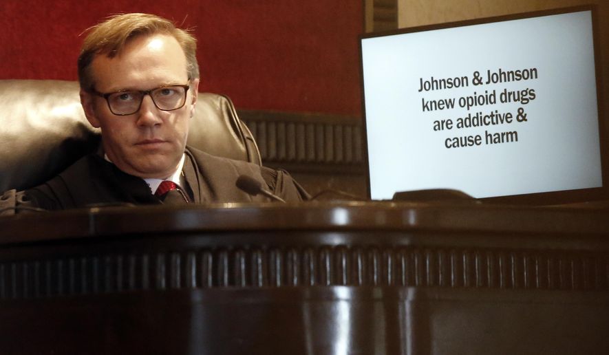 FILE - In this May 28, 2019, file photo, Judge Thad Balkman listens in Norman, Okla., during opening arguments as a slide from the state's presentation is displayed on a monitor in Oklahoma's trial against drugmakers blamed for contributing to the opioid crisis. Judge Balkman reduces amount Johnson & Johnson must pay state to help clean up opioid crisis by $107 million to $465 million on Friday Nov. 15, 2019. (AP Photo/Sue Ogrocki, File)