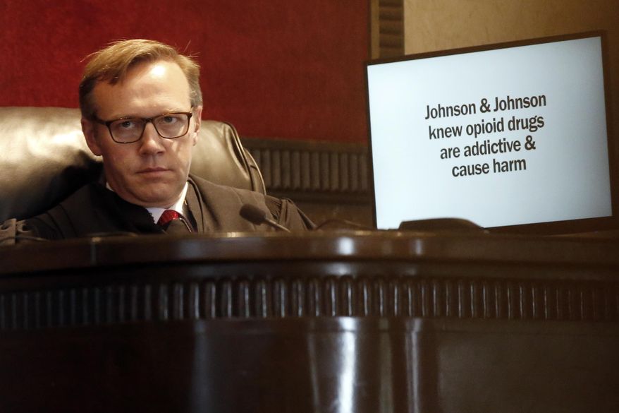 FILE - In this May 28, 2019, file photo, Judge Thad Balkman listens in Norman, Okla., during opening arguments as a slide from the state's presentation is displayed on a monitor in Oklahoma's trial against drugmakers blamed for contributing to the opioid crisis. Judge Balkman reduces amount Johnson & Johnson must pay state to help clean up opioid crisis by $107 million to $465 million on Friday Nov. 15, 2019. (AP Photo/Sue Ogrocki, File)
