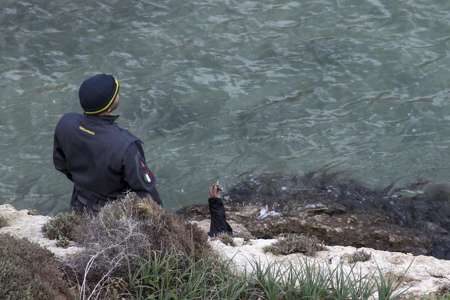 An arm of a migrant is seen as a border police officer stands by a woman's body recovered at sea near the Sicilian island of Lampedusa, southern Italy, Sunday, Nov. 24, 2019. Italian news reports say the Italian coast guard has recovered seven bodies of migrants near Lampedusa and kept up its search Sunday of rough seas for as many as 13 other migrants feared missing after their boat capsized on Saturday. (AP Photo/Mauro Seminara)
