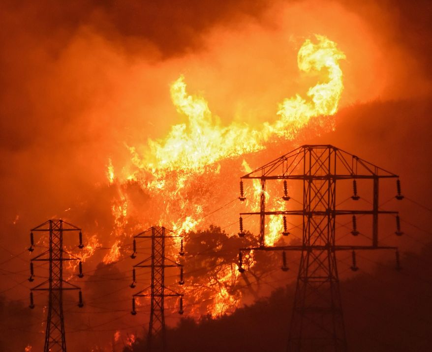 FILE - In this Dec. 16, 2017, file photo provided by the Santa Barbara County Fire Department, flames burn near power lines in Sycamore Canyon near West Mountain Drive in Montecito, Calif. California says sparks from power lines and other electrical equipment caused many of the state’s major wildfires in 2017 and 2018. Federal officials have awarded $176 million over several years to help states and territories bury power lines. (Mike Eliason/Santa Barbara County Fire Department via AP, File)