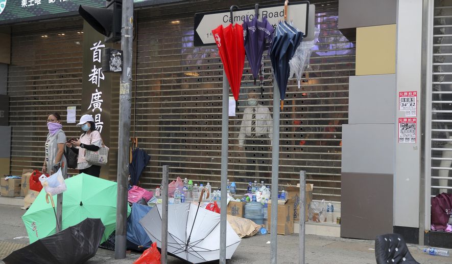 People stand near a shop closed in the aftermath of protests in Hong Kong, Monday, Nov. 18, 2019. Hong Kong police using tear gas and rubber bullets fought off protesters Monday as they tried to break through a police cordon that is trapping hundreds of them on a university campus. (AP Photo/Kin Cheung)