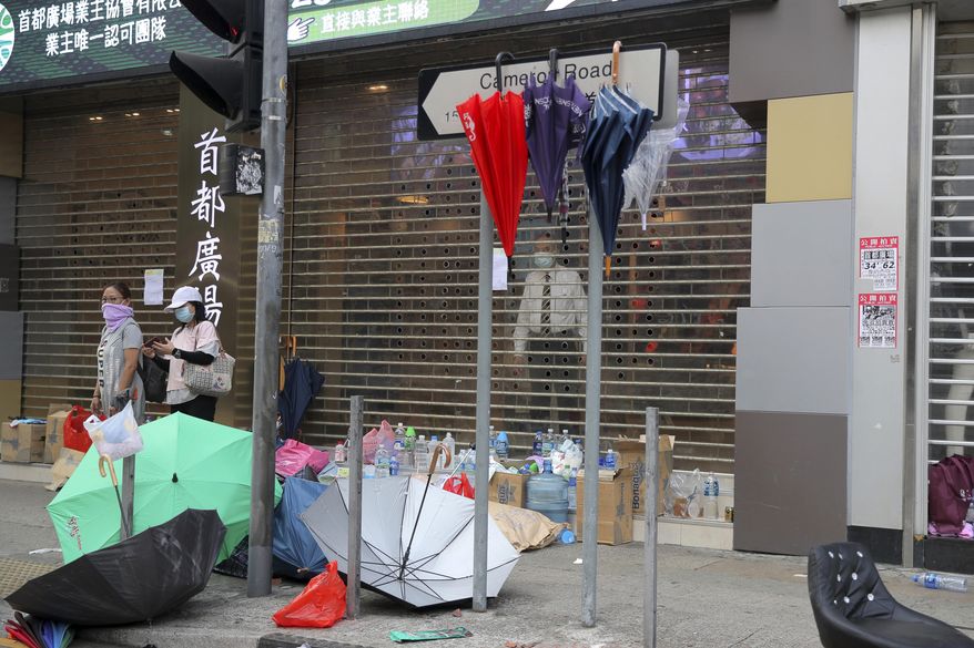 People stand near a shop closed in the aftermath of protests in Hong Kong, Monday, Nov. 18, 2019. Hong Kong police using tear gas and rubber bullets fought off protesters Monday as they tried to break through a police cordon that is trapping hundreds of them on a university campus. (AP Photo/Kin Cheung)