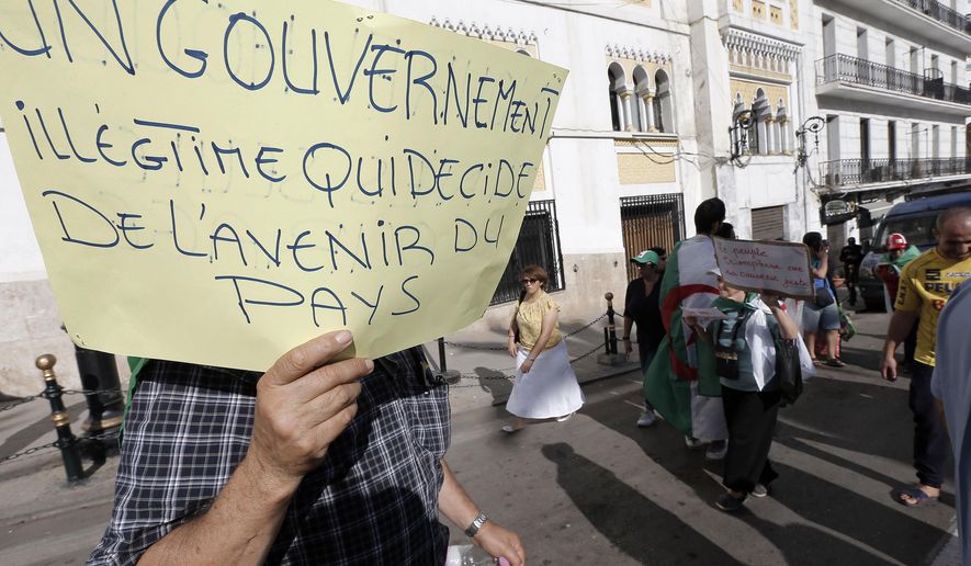 FILE - In this Oct. 18, 2019, file photo, Algerians take part in a protest against the government in Algiers. Algeria's presidential campaign is in trouble. Candidates are struggling to fill rally venues, two campaign chiefs have quit, voters have pelted candidates' headquarters with tomatoes and eggs, and a 9-month-old pro-democracy movement calls the whole thing a sham. Poster reads "An illegitimate Government that decides the Future of the Country." (AP Photo/Toutik Doudou, File)