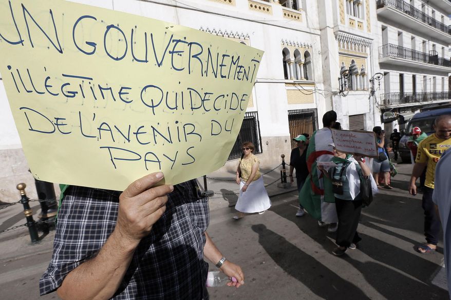 FILE - In this Oct. 18, 2019, file photo, Algerians take part in a protest against the government in Algiers. Algeria's presidential campaign is in trouble. Candidates are struggling to fill rally venues, two campaign chiefs have quit, voters have pelted candidates' headquarters with tomatoes and eggs, and a 9-month-old pro-democracy movement calls the whole thing a sham. Poster reads "An illegitimate Government that decides the Future of the Country." (AP Photo/Toutik Doudou, File)