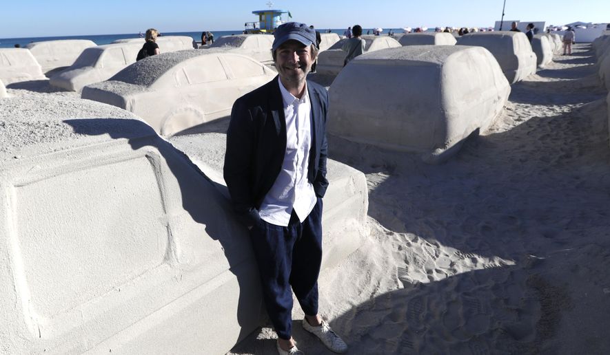Artist Leandro Erlich, of Argentina, poses with his work featuring cars sculpted in sand stuck in a traffic jam, titled Order of Importance, displayed as part of Miami Art Week, Tuesday, Dec. 3, 2019, in Miami Beach, Fla. Erlich was commissioned by the city of Miami Beach to create the work, which was unveiled during Art Basel Miami. (AP Photo/Lynne Sladky)