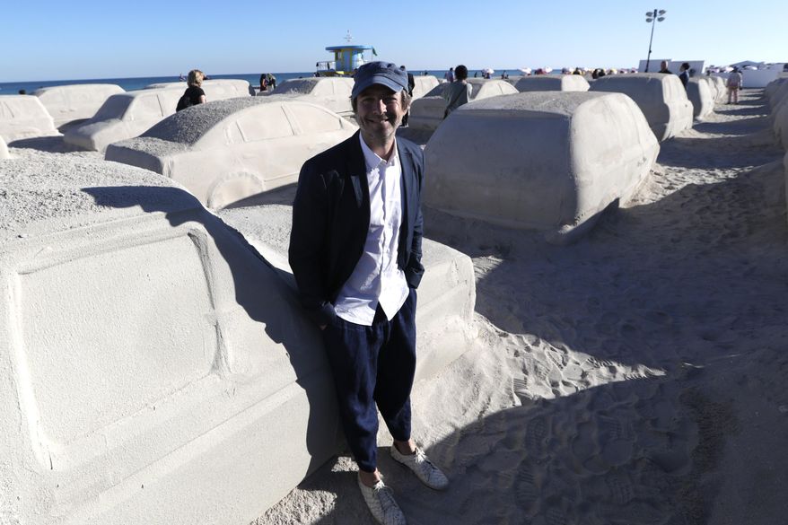 Artist Leandro Erlich, of Argentina, poses with his work featuring cars sculpted in sand stuck in a traffic jam, titled Order of Importance, displayed as part of Miami Art Week, Tuesday, Dec. 3, 2019, in Miami Beach, Fla. Erlich was commissioned by the city of Miami Beach to create the work, which was unveiled during Art Basel Miami. (AP Photo/Lynne Sladky)